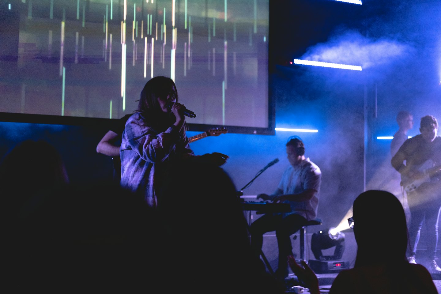 Band performing on stage in front of a digital screen.